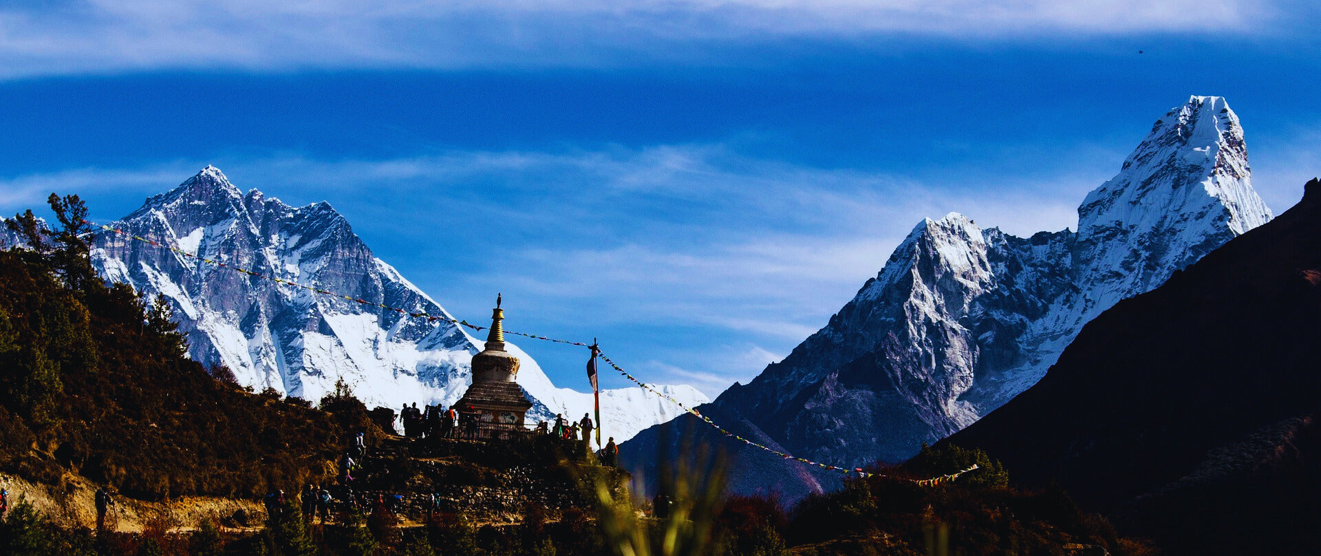 Buddhistischer Stupa im Himalaya-Gebirge mit schneebedeckten Bergen und blauem Himmel im Hintergrund, umgeben von Gebetsfahnen – spirituelles Symbol und beeindruckende Naturlandschaft